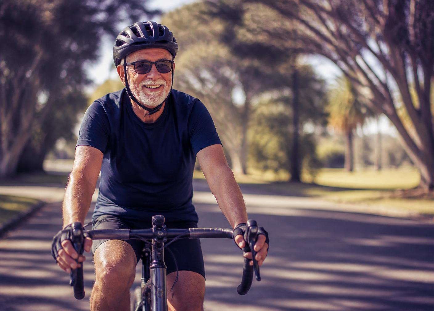 Smiling man in his seventies cycling through a sunlit park